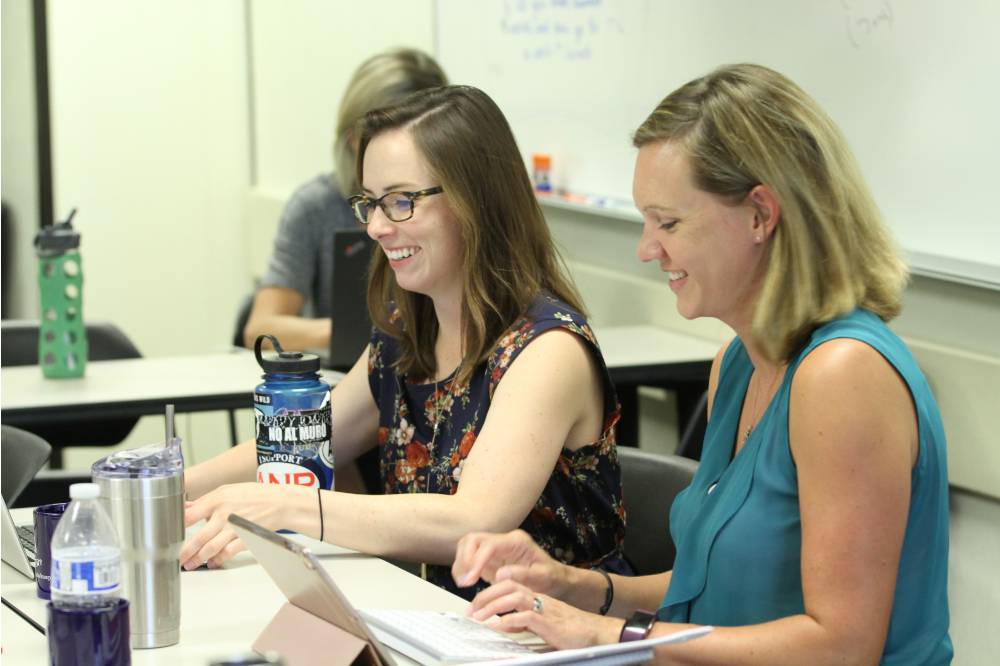 Two teacher fellows work on their computers during the summer institute.